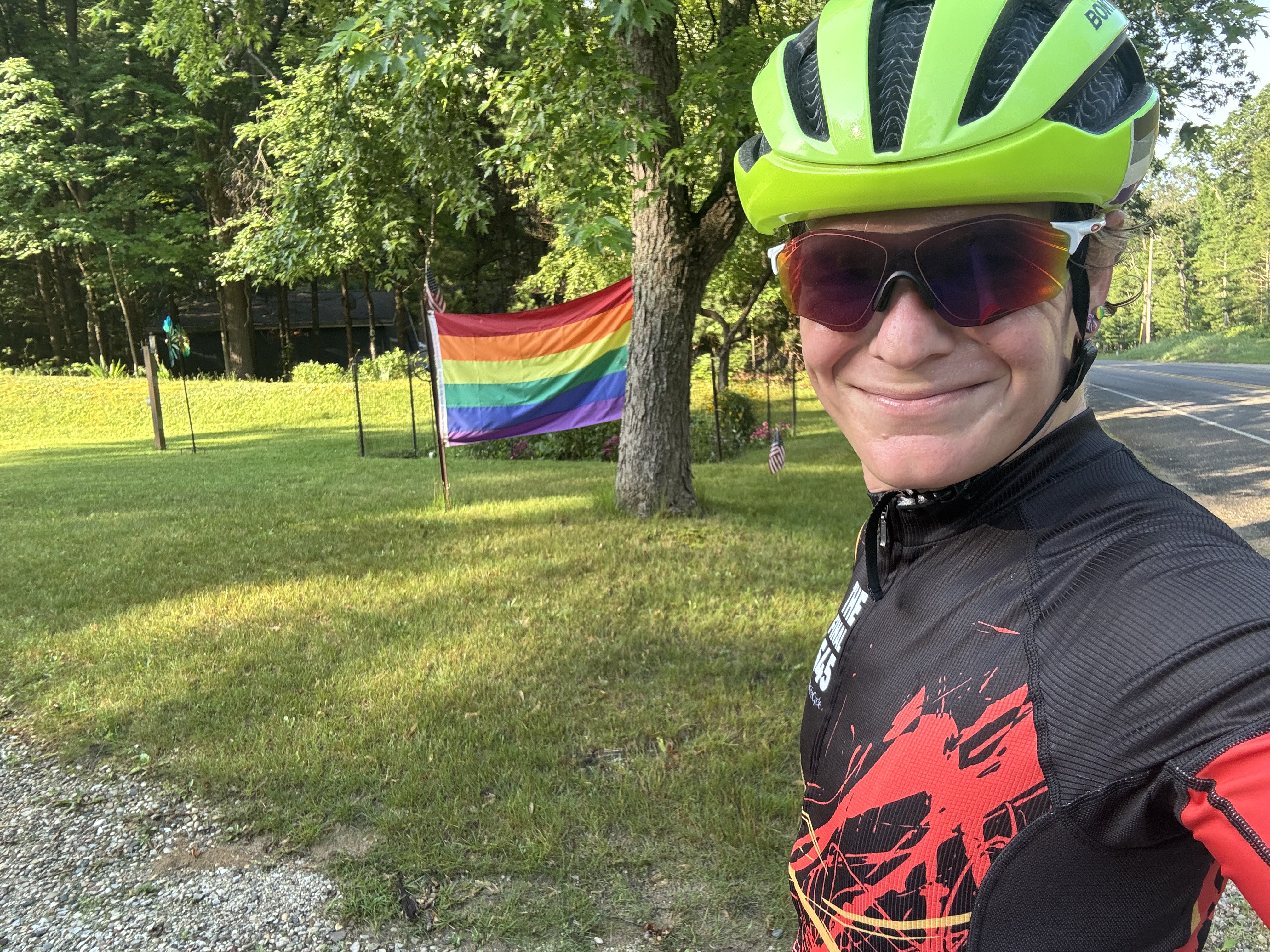 Rider selfie in helmet next to a pride flag by the roadside.