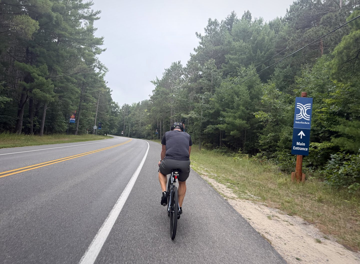 A Pedal for Pride cyclist riding past the Interlochen main entrance sign on Day 1.