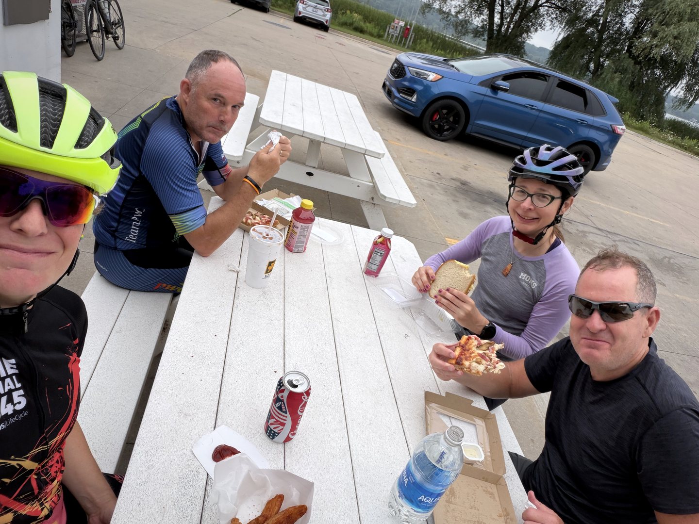 Four riders having lunch at a roadside picnic table.