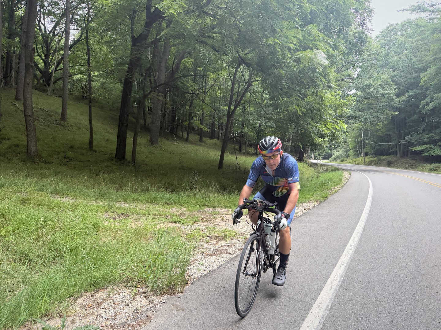 A cyclist rounding a curve on a tree-lined paved trail.