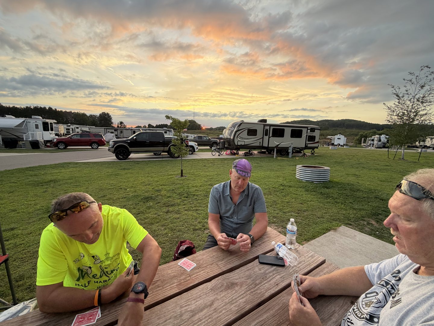 Team members gathered at a picnic table beneath a colorful campground sunset.