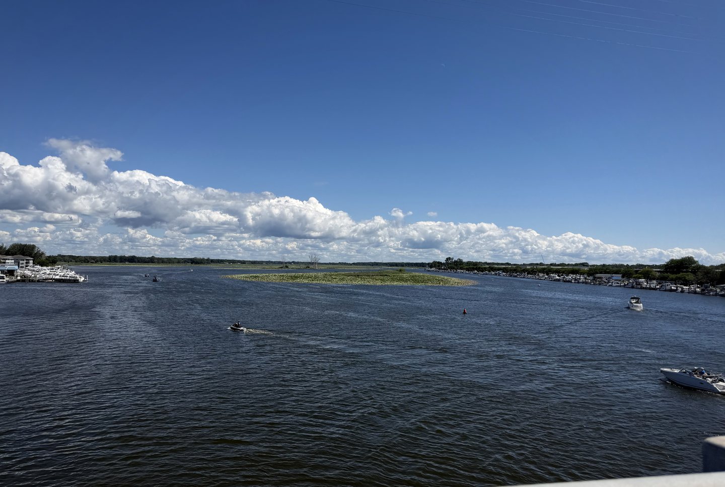 Boats moving across a blue lake beneath bright clouds.
