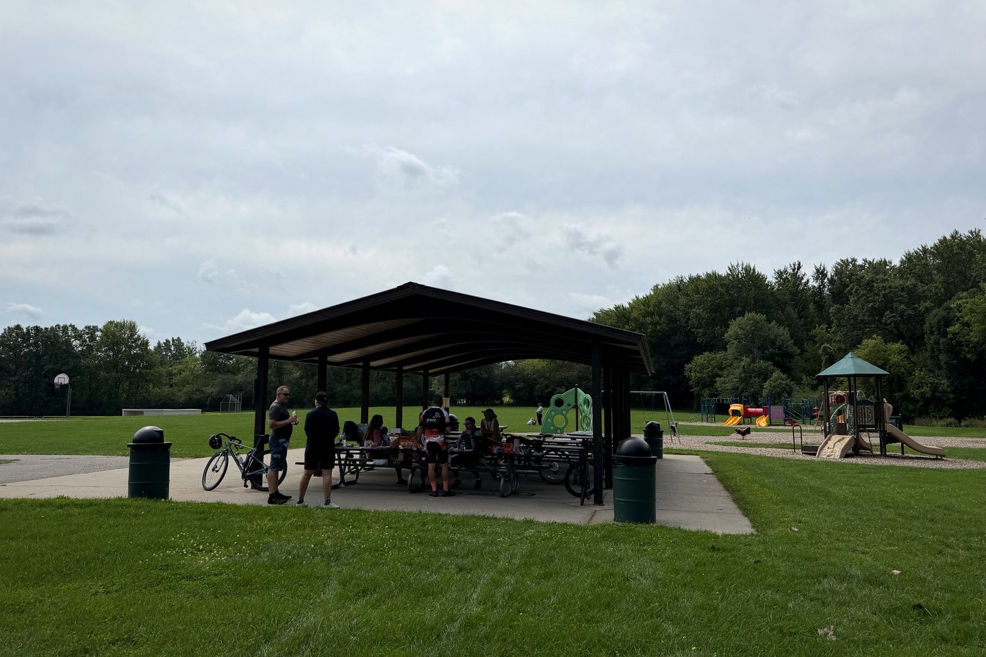 Pedal for Pride riders and roadies sharing lunch beneath a park pavilion in 2026.