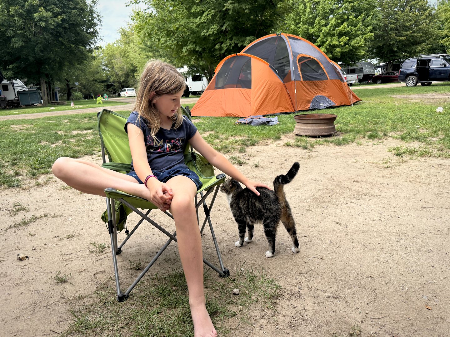 A young roadie petting a campground cat beside a tent.