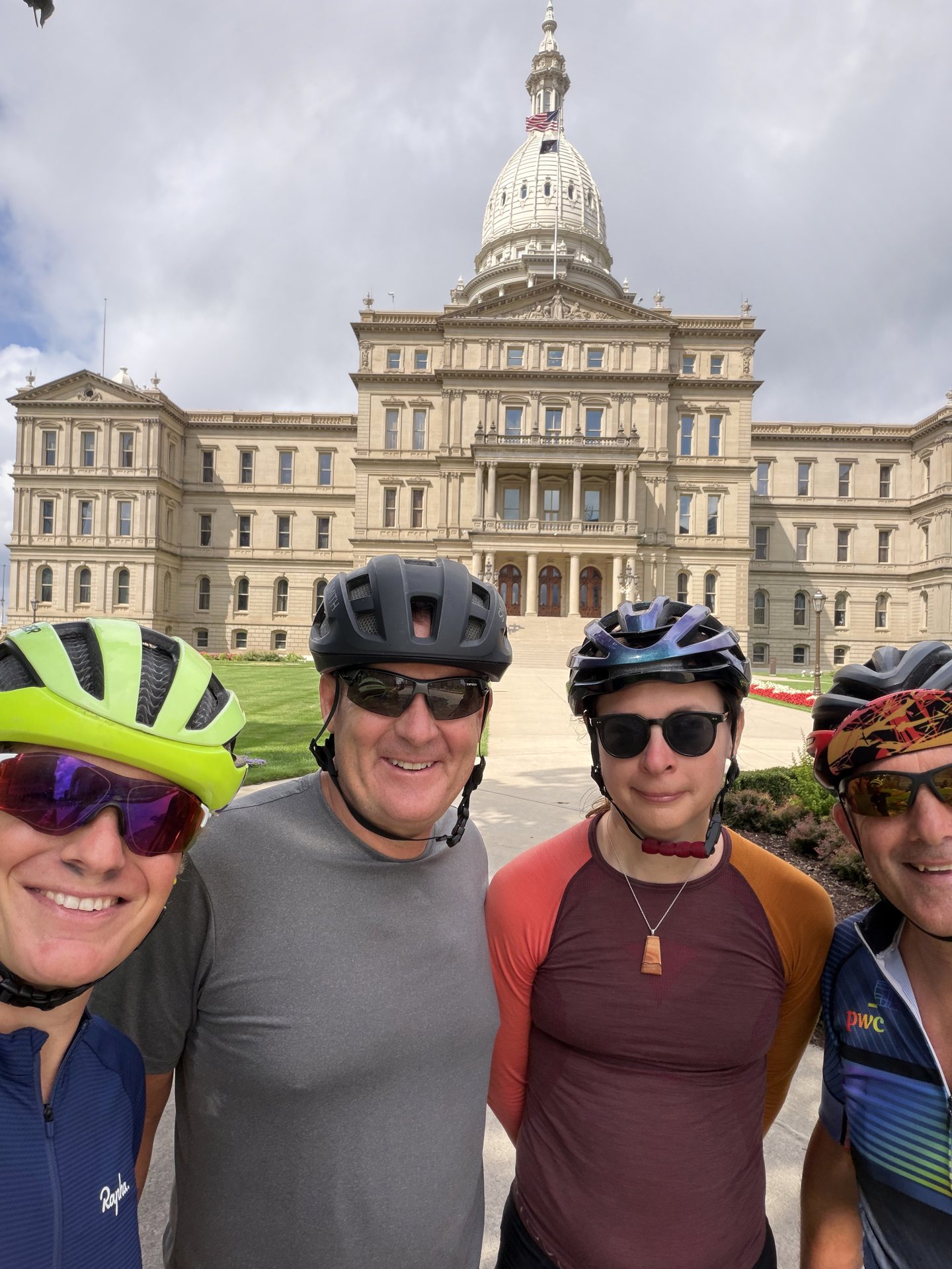 Four riders smiling together in front of the Michigan State Capitol.