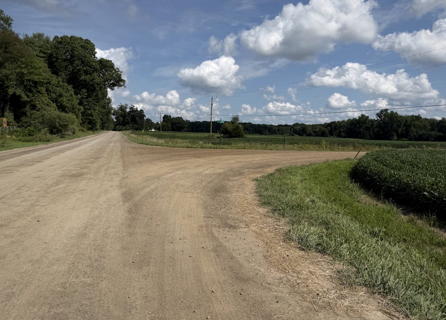 A gravel road curving through open farmland beneath bright clouds.