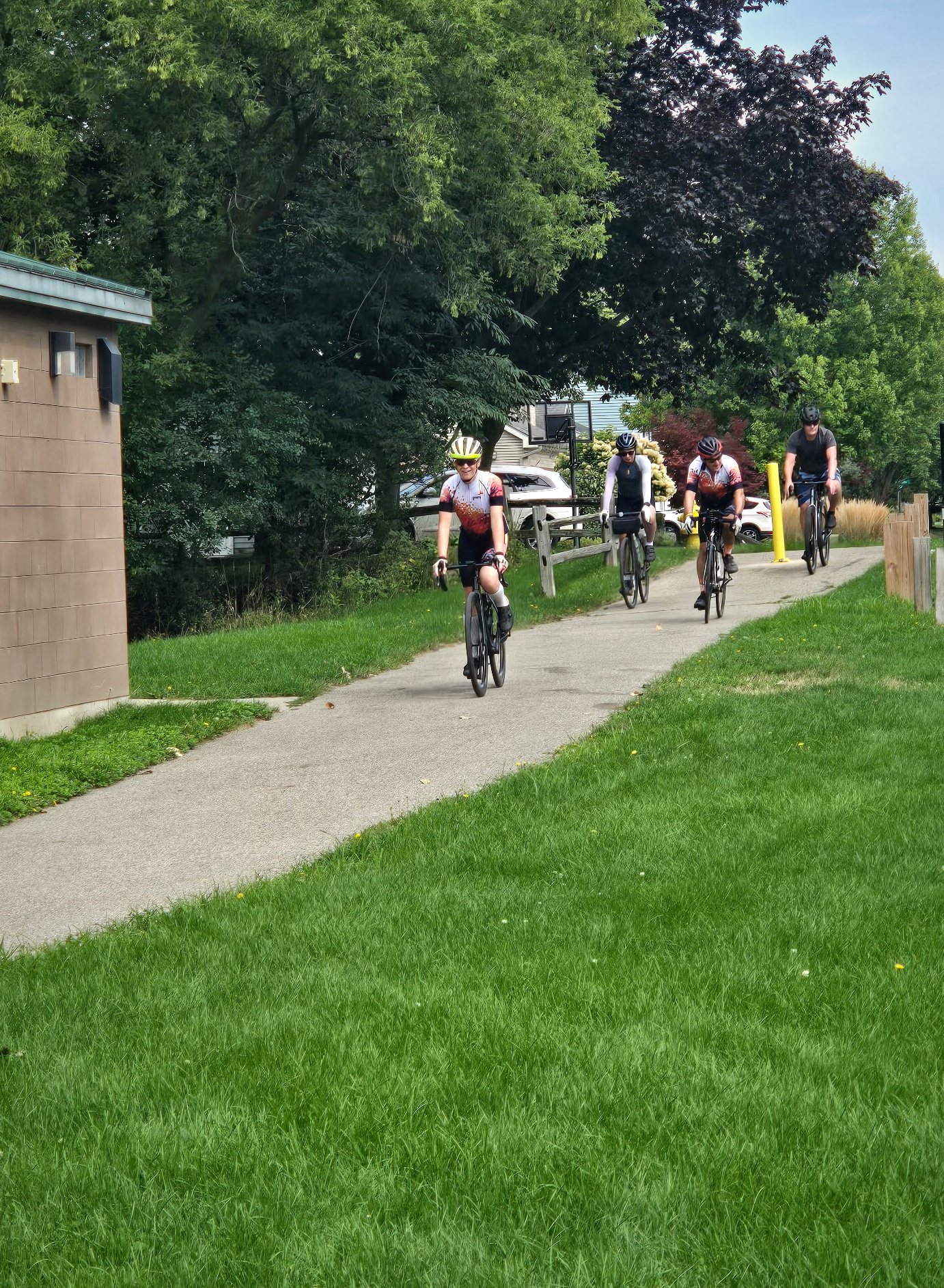 Four cyclists riding together on a green neighborhood trail.