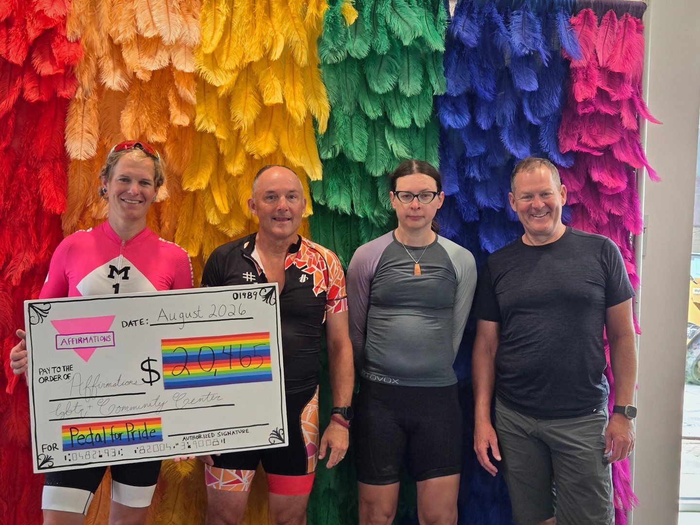Four riders holding the Pedal for Pride donation check inside Affirmations.