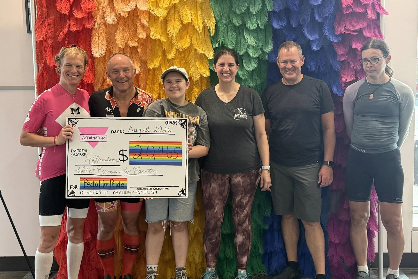Pedal for Pride riders and Day 5 participants holding the $20,465 donation check at Affirmations in 2026.